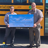 Two men holding a large check in front of a bus