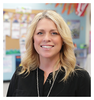 Happy teacher proudly standing in front of her classroom